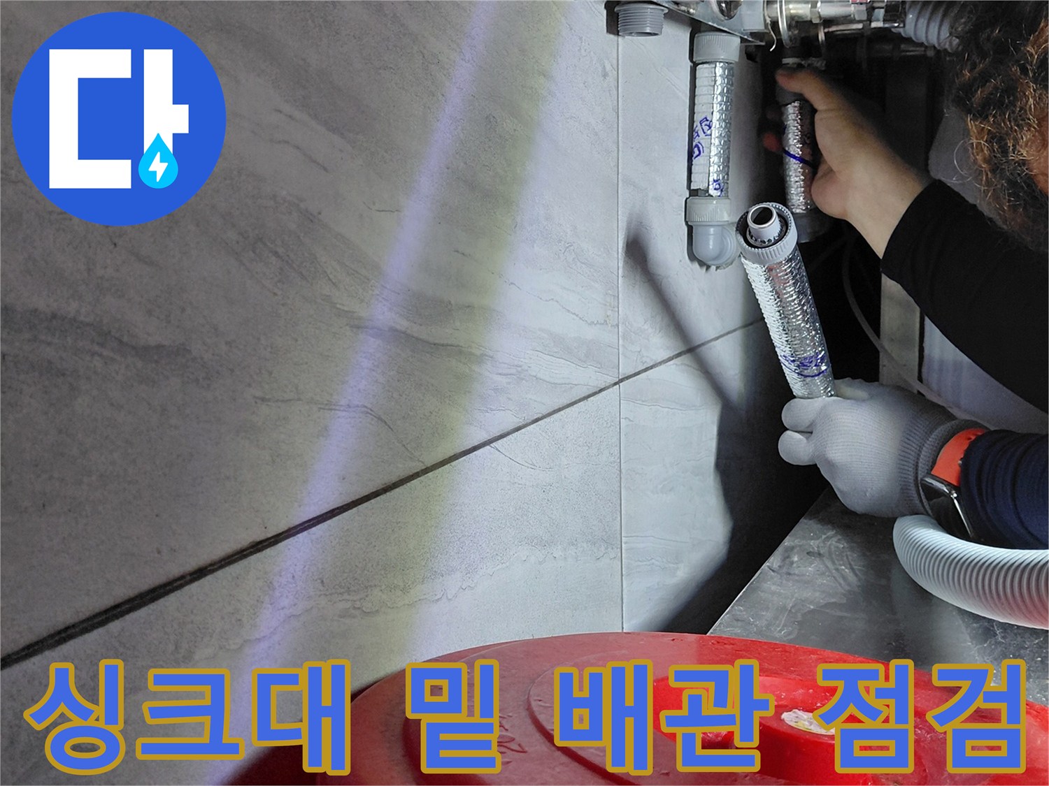 주방 싱크대 하부의 에이콘 배관 연결 부위를 정밀하게 점검하는 모습