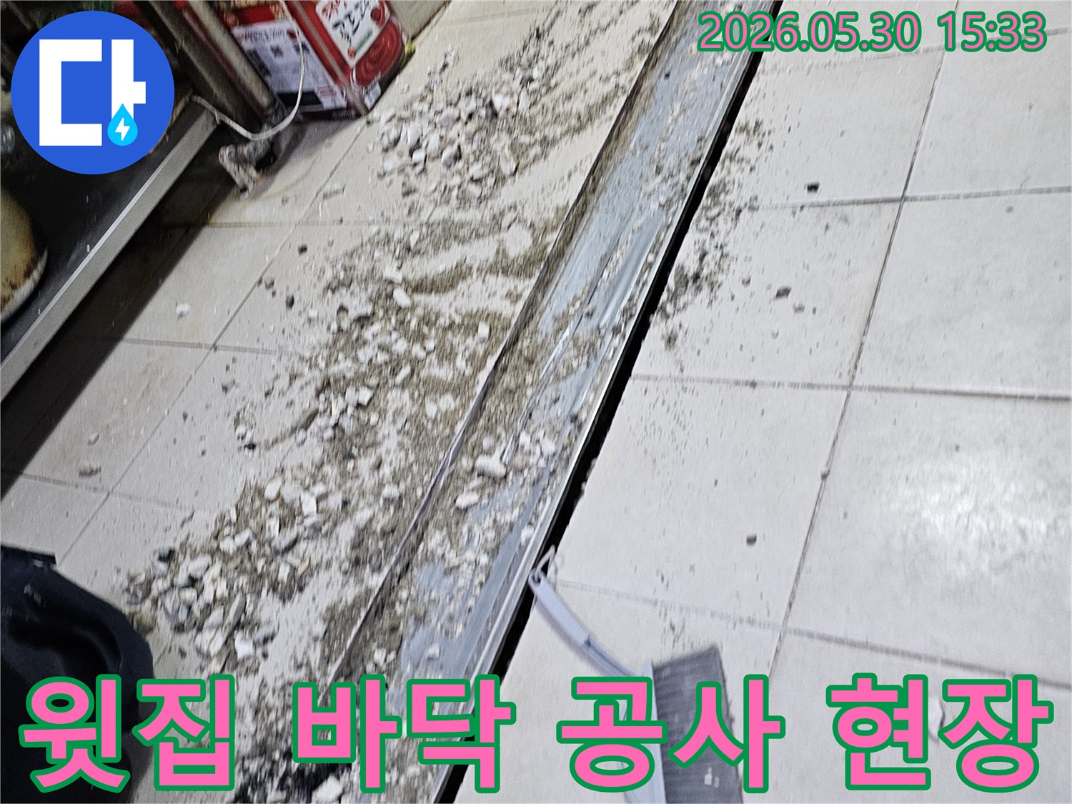 누수 공사 현장에서-바닥 타일 파쇄 후-발생한 잔해물과-청소 도구가-함께 보이는-작업 진행 모습입니다.