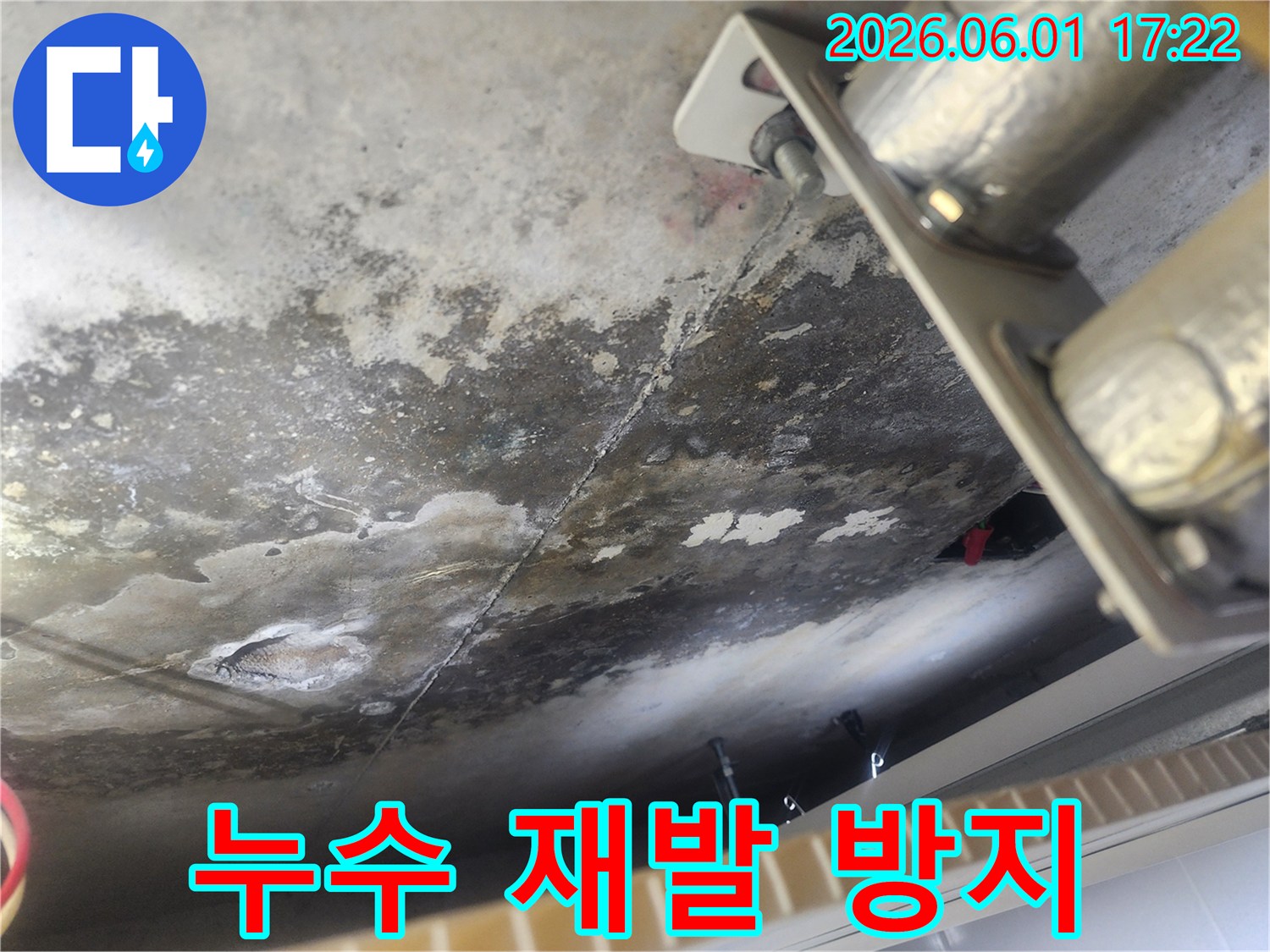 누수로 인해 얼룩지고 젖은 콘크리트 천장-배관 지지대 주변의 물기 흔적과 오염