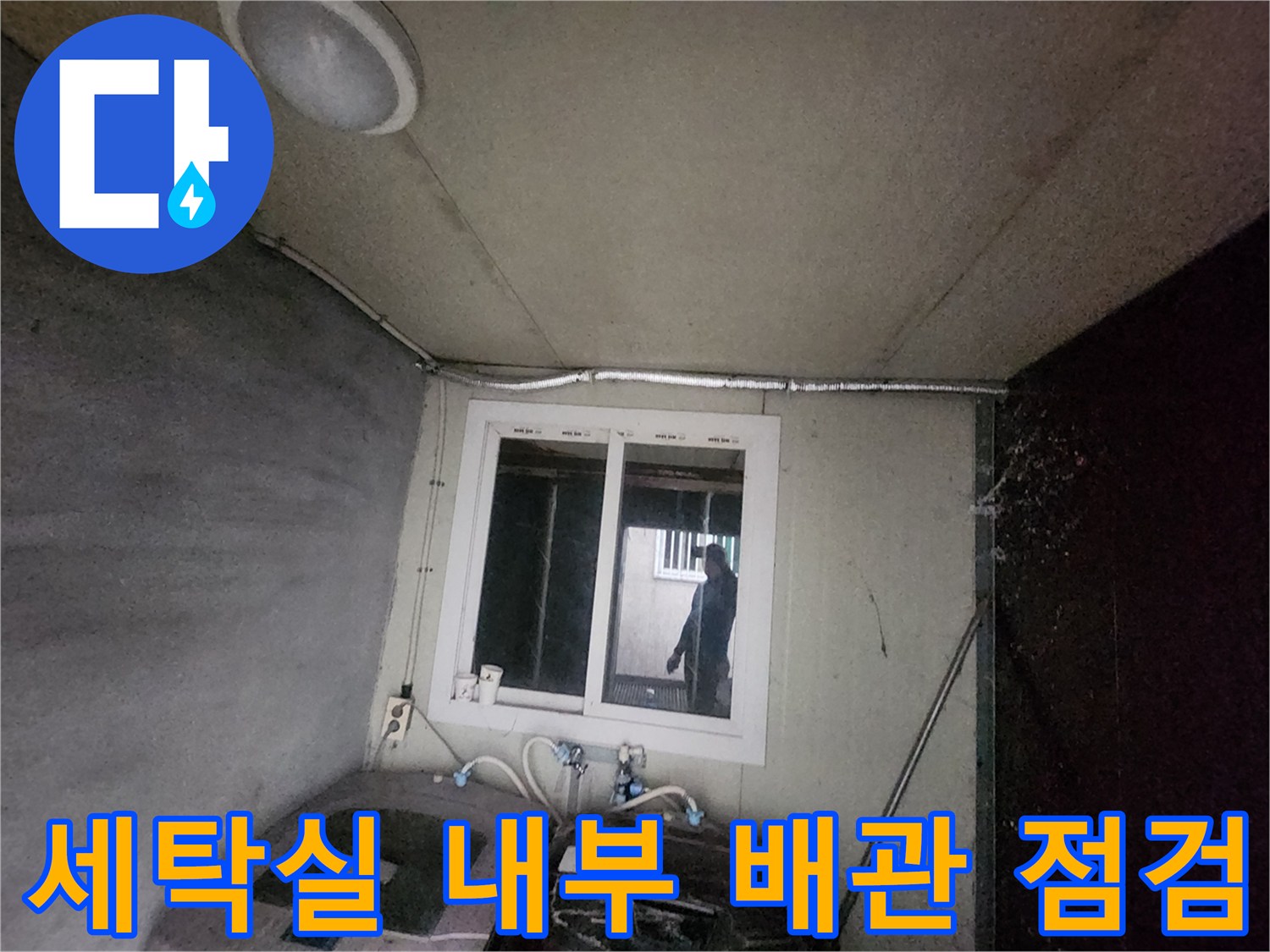 세탁기 옆에 위치한 노출 배관과 창문이 있는 공간의 모습