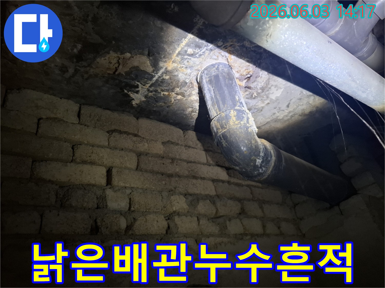 지하의 낡은 배관에서-물이 새어 나와-벽돌 벽에 스며든-누수 자국을-조명으로 비추어-면밀히 검사하는 모습