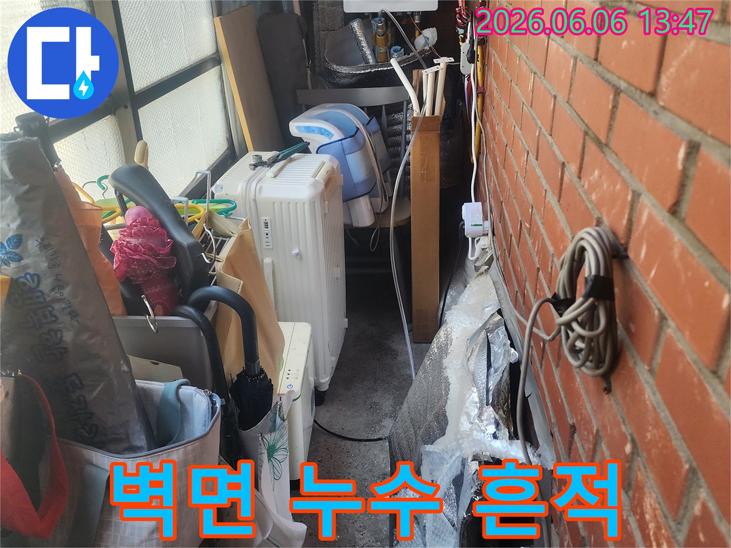 벽돌-벽-아래-복잡하게-얽힌-배관과-생활-용품들-사이에서-발견된-누수-흔적을-보여주는-사진