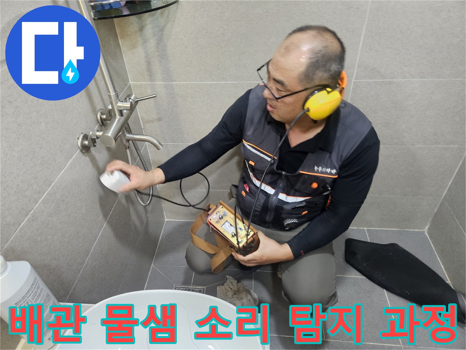 귀 보호용 헤드셋을 착용한 작업자가 청음 장비로 화장실 배관의 누수 지점을 찾는 장면입니다.