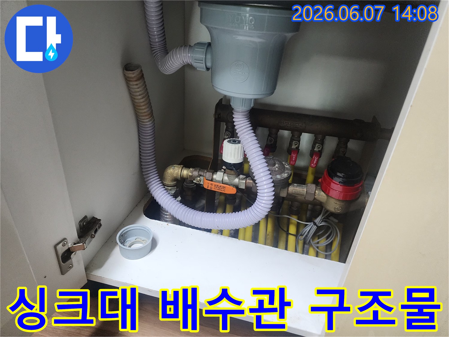 하얀색 싱크대 하부장에 설치된 배수 호스와 수도 밸브 상세 사진입니다.