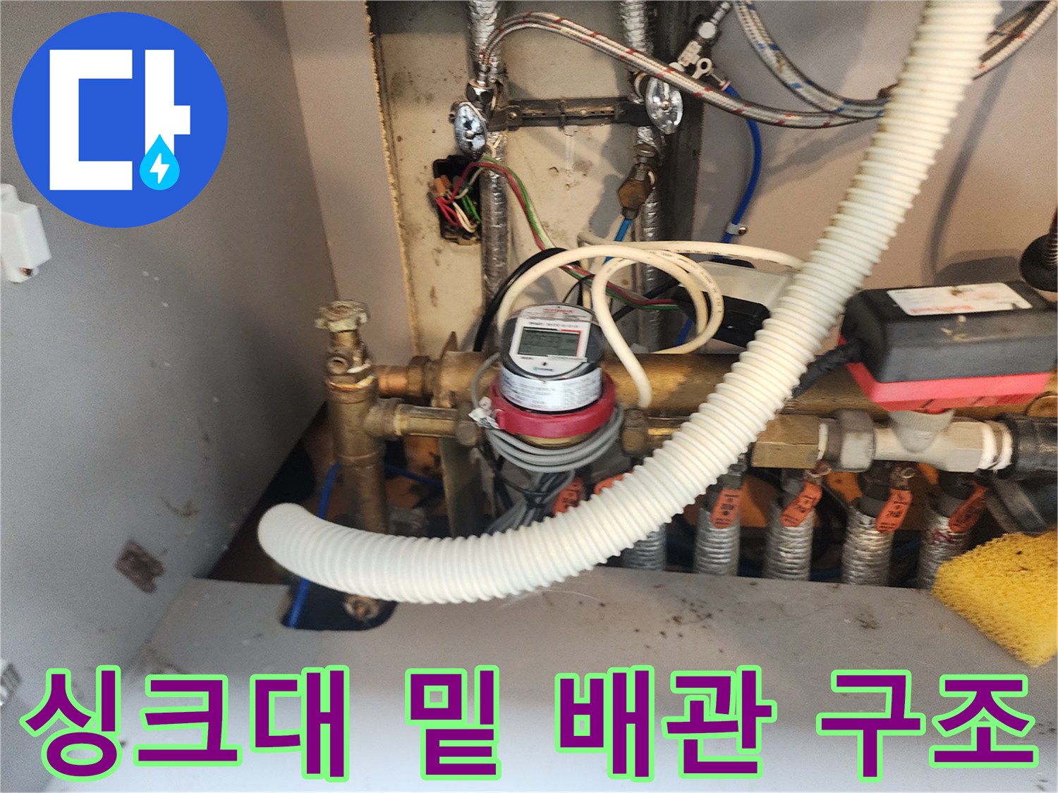 싱크대 아래쪽의 복잡한 금속 배관과 계량기 모습입니다.