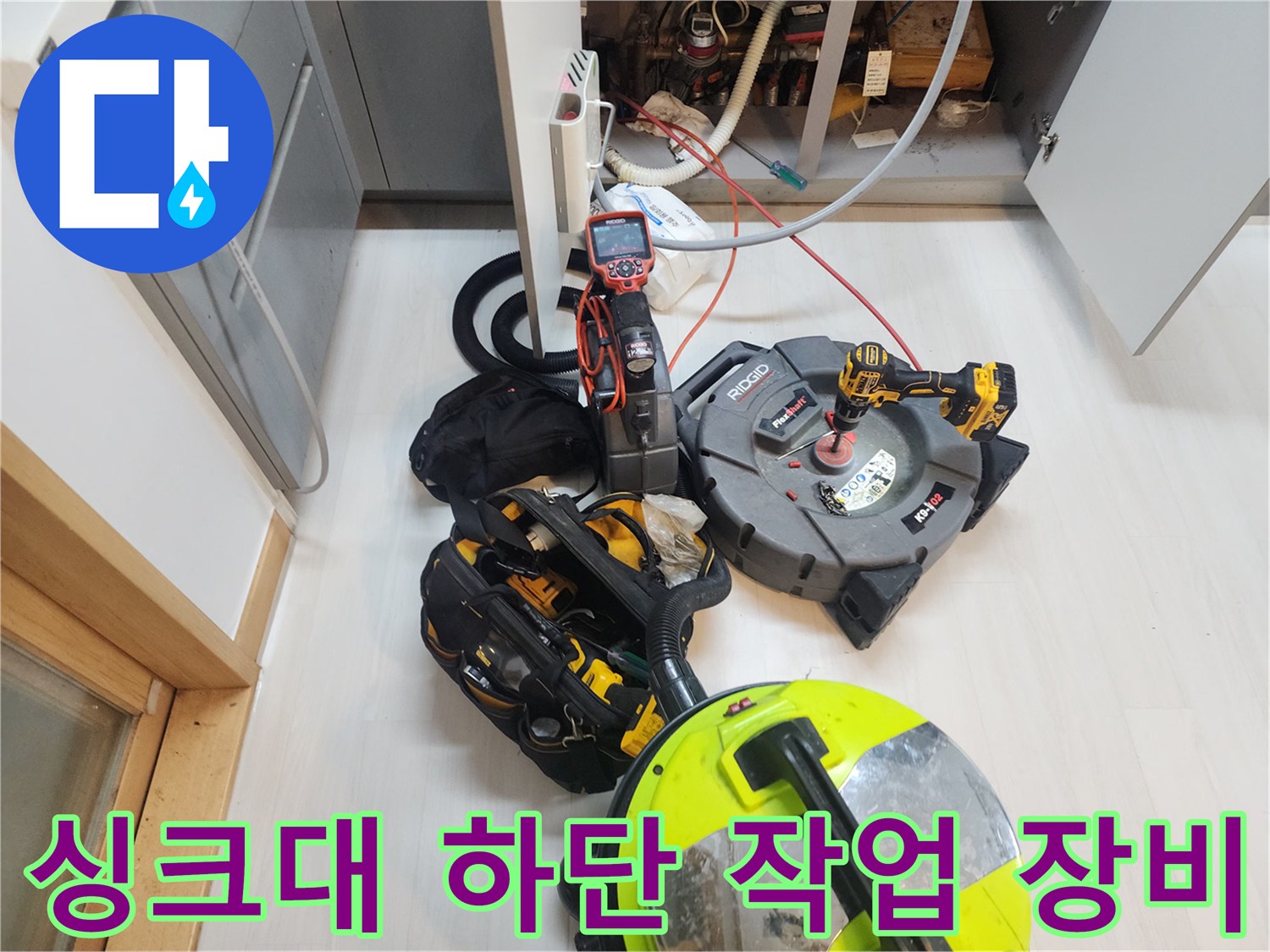 주방 싱크대 하부장 아래에 배치된 배관 스케일링 장비와 석션기 모습입니다.