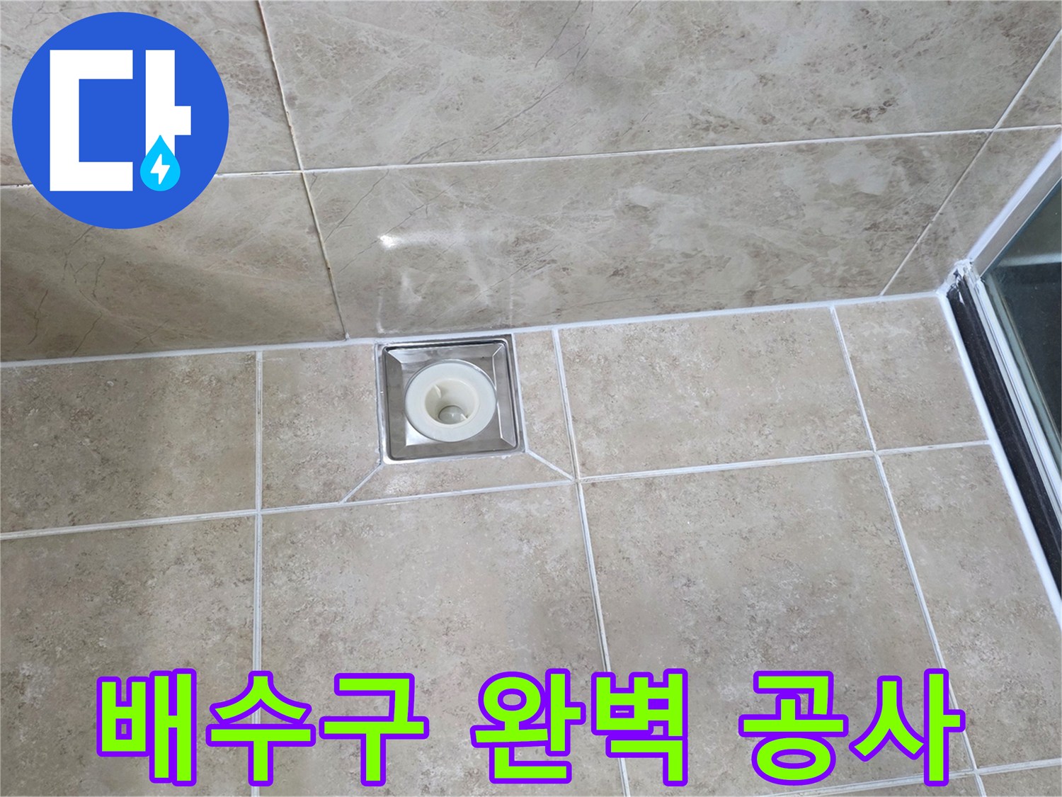 베이지색 타일 바닥에 설치된-금속 사각 배수구의 모습으로-주변 타일과 줄눈의 마감 상태를 보여줍니다