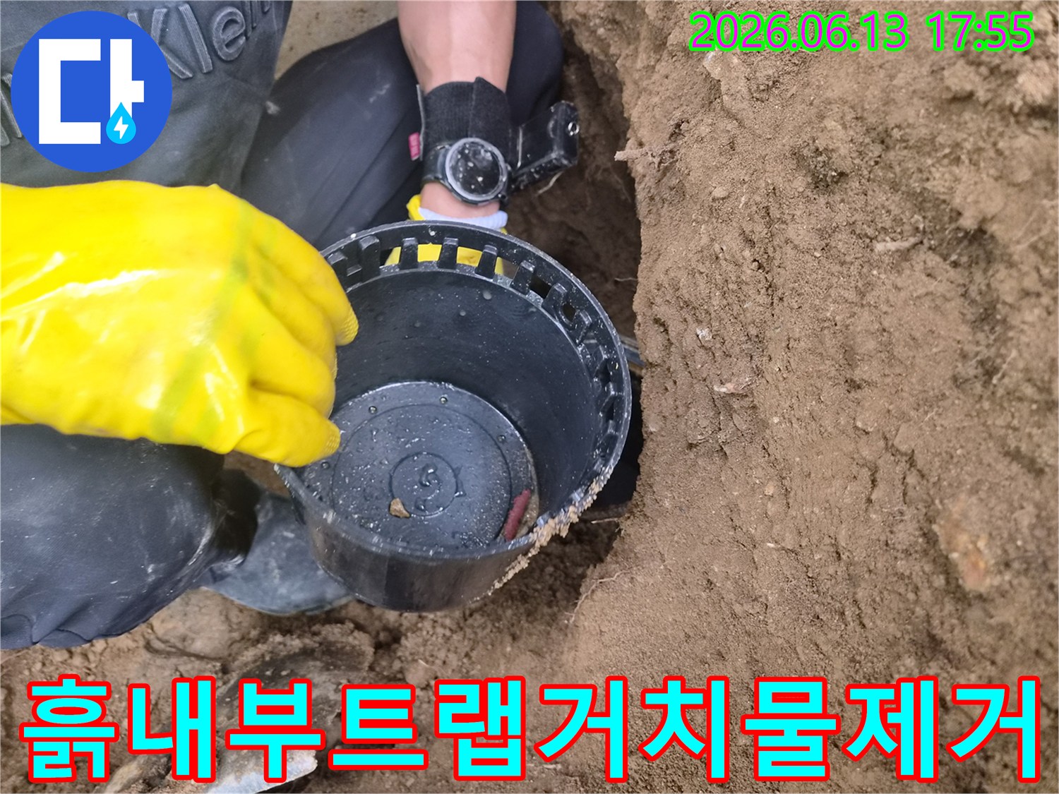 장갑을 착용한 작업자가 땅에서 파낸 트랩 모양의 배관 부품을 들어 올린 모습