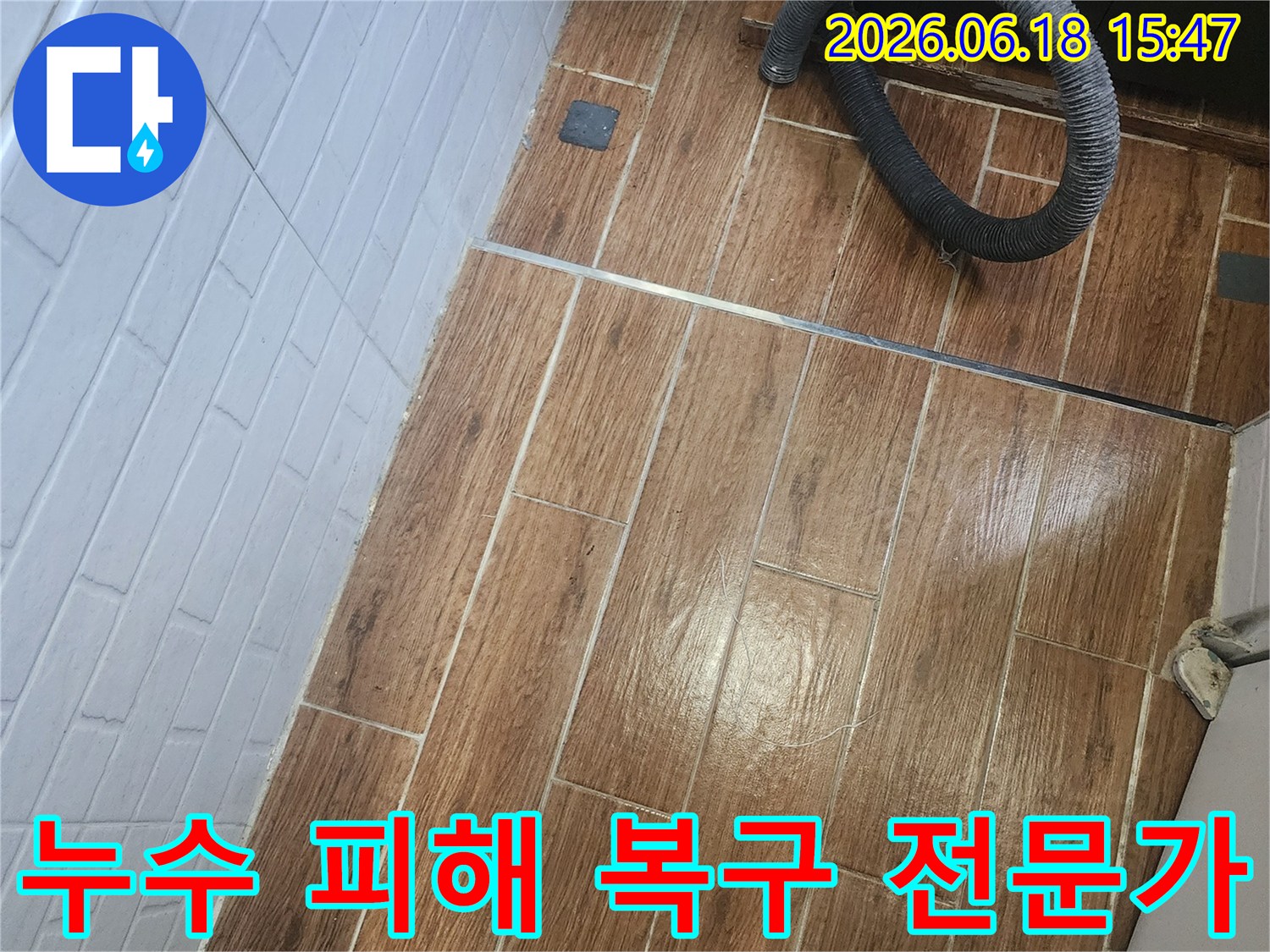염창동 아파트에서 누수 피해를 복구하기 위해 전문가가 현장을 방문하여 탐지 작업 중인 사진입니다-바닥 타일 위에 검은색 호스가 놓여 있습니다.