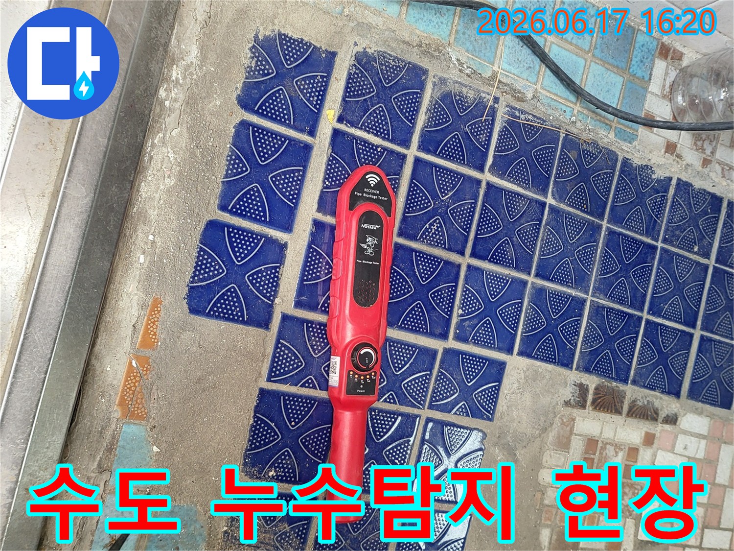 파란색 타일이 뜯겨나간 욕실 바닥에 놓인-붉은색 누수탐지 장비가-수도 배관 누수 지점을 찾는 중인 모습