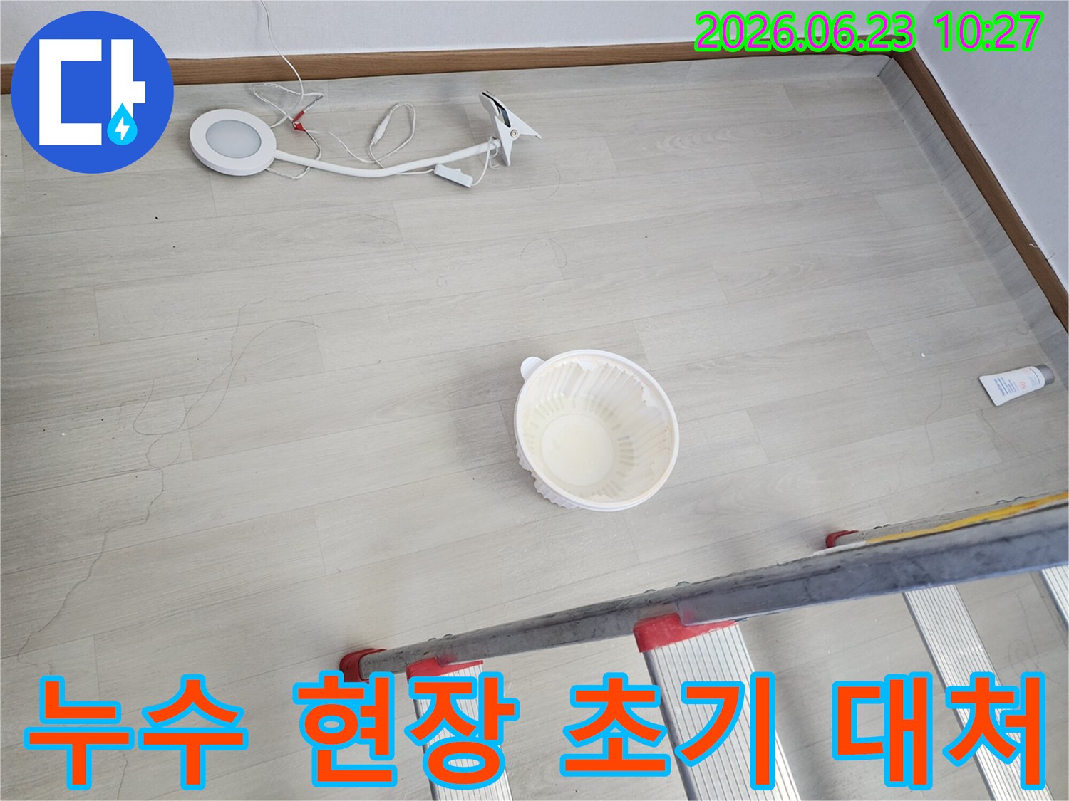 천장에서 물이 떨어져 바닥에 놓인 물받이 그릇과-누수 지점 확인을 위한 사다리-작업용 조명 장비가 함께 보이는-누수 공사 전 현장 모습입니다