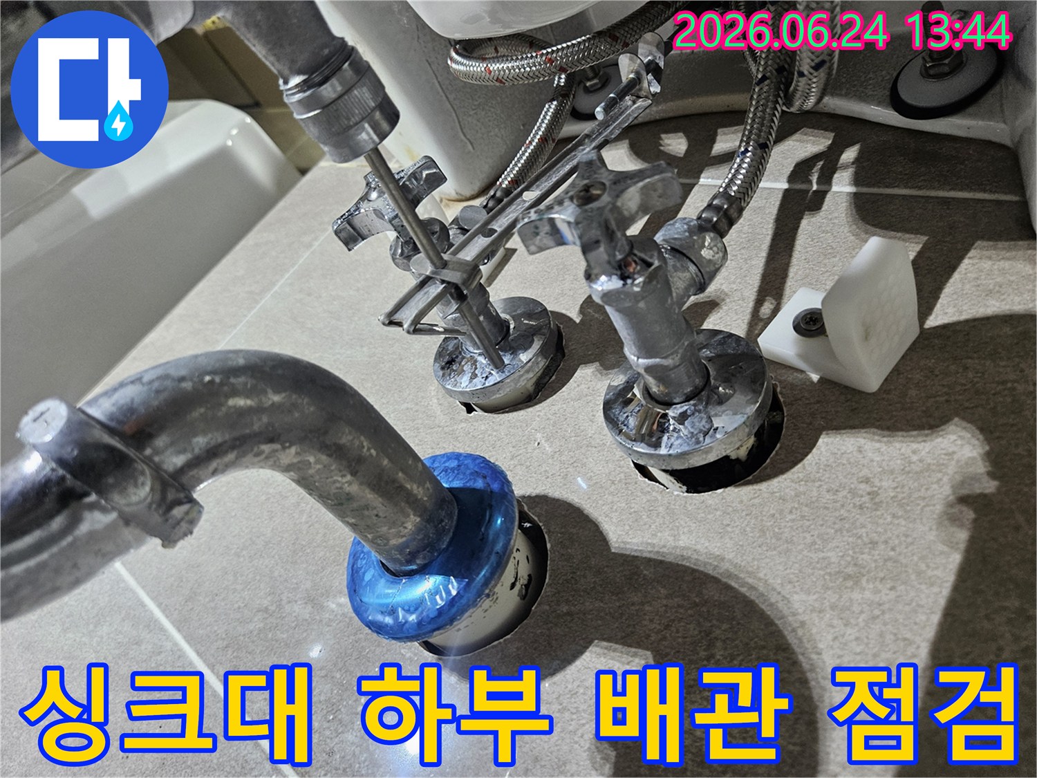 이 사진은 싱크대 하부의 복잡한 배관과 수전 연결부를-보여주며 누수 점검을-위해 작업 중인-모습을-담고 있습니다.