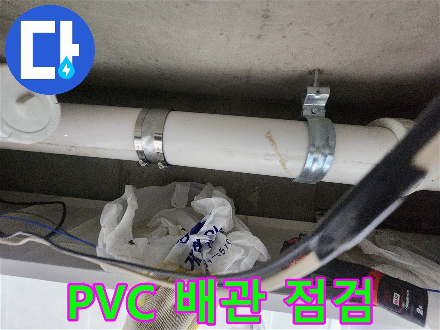천장에 고정된 PVC 배관과 금속 클램프의 근접 촬영 사진입니다.