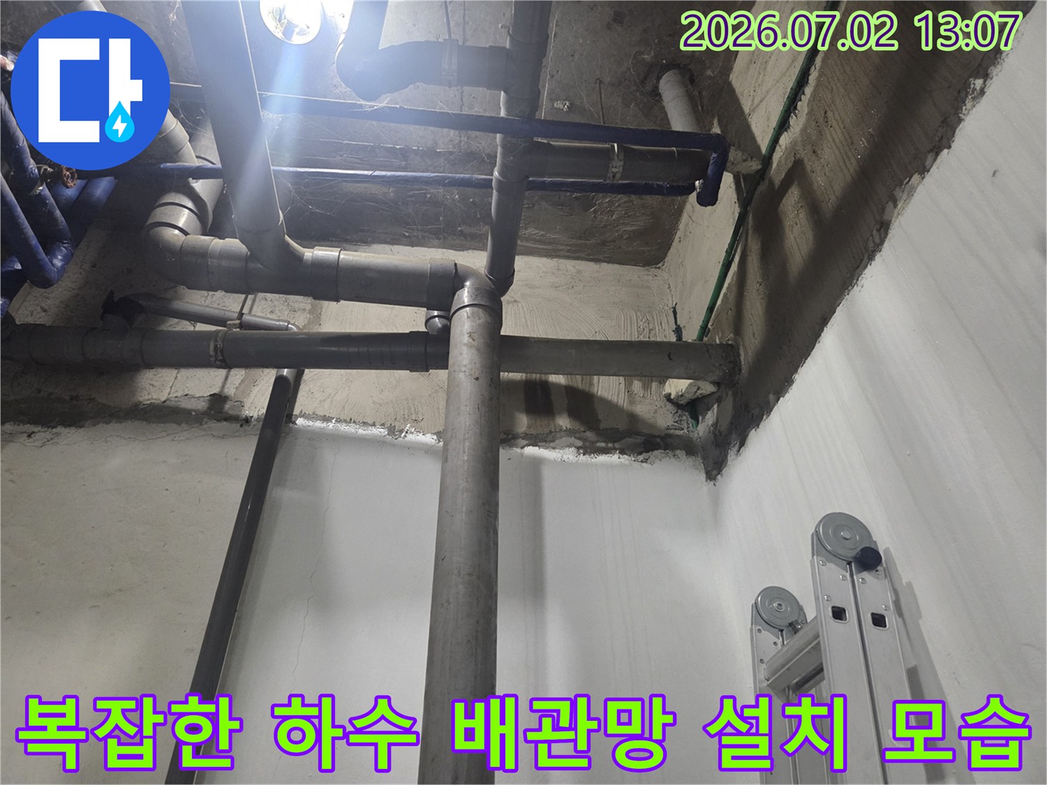 지하실 천장에 수평과 수직으로 교차 배치된 회색 생활하수 파이프 라인