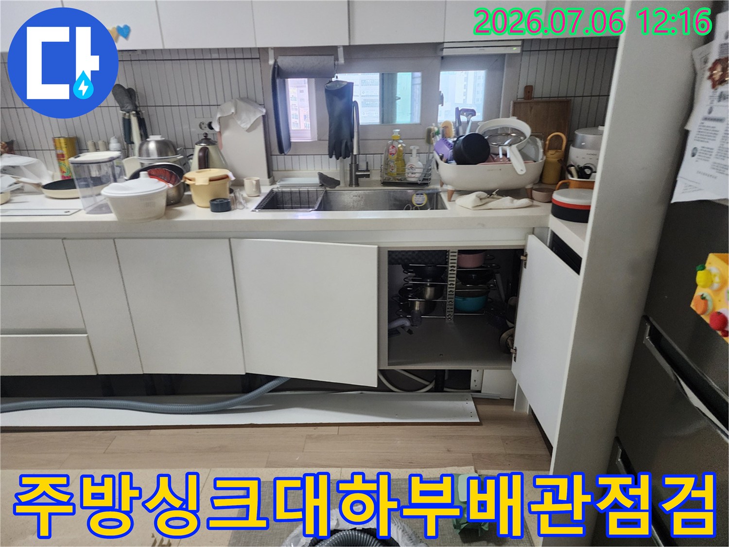 싱크대 하부장 문을 열고 배수 호스와 연결 부위를 점검하는 모습