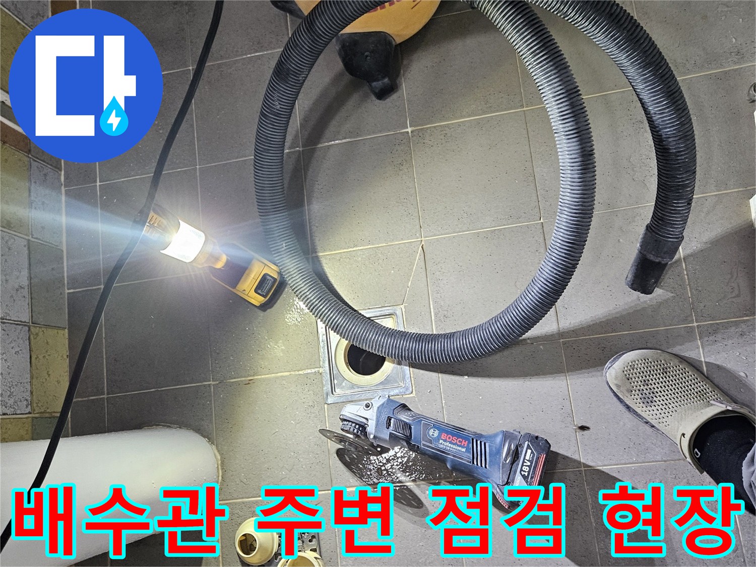 욕실 바닥의 배수구와 작업용 전동 공구가 놓여 있는 모습입니다.