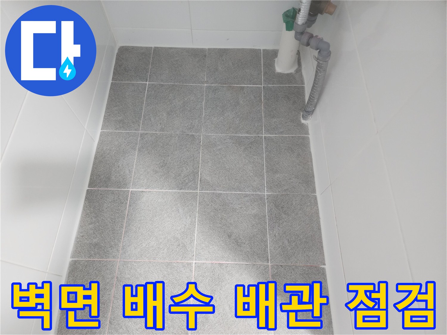 하얀색 배관과 회색 배수 호스가 연결된 벽면 하단부