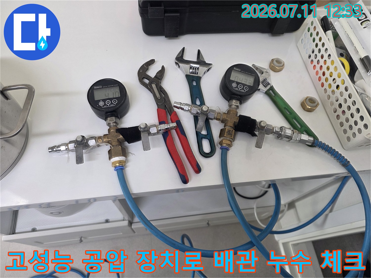 전문가용 게이지와 파란색 고압 호스를 이용해 배관의 기밀성을 점검하는 장면