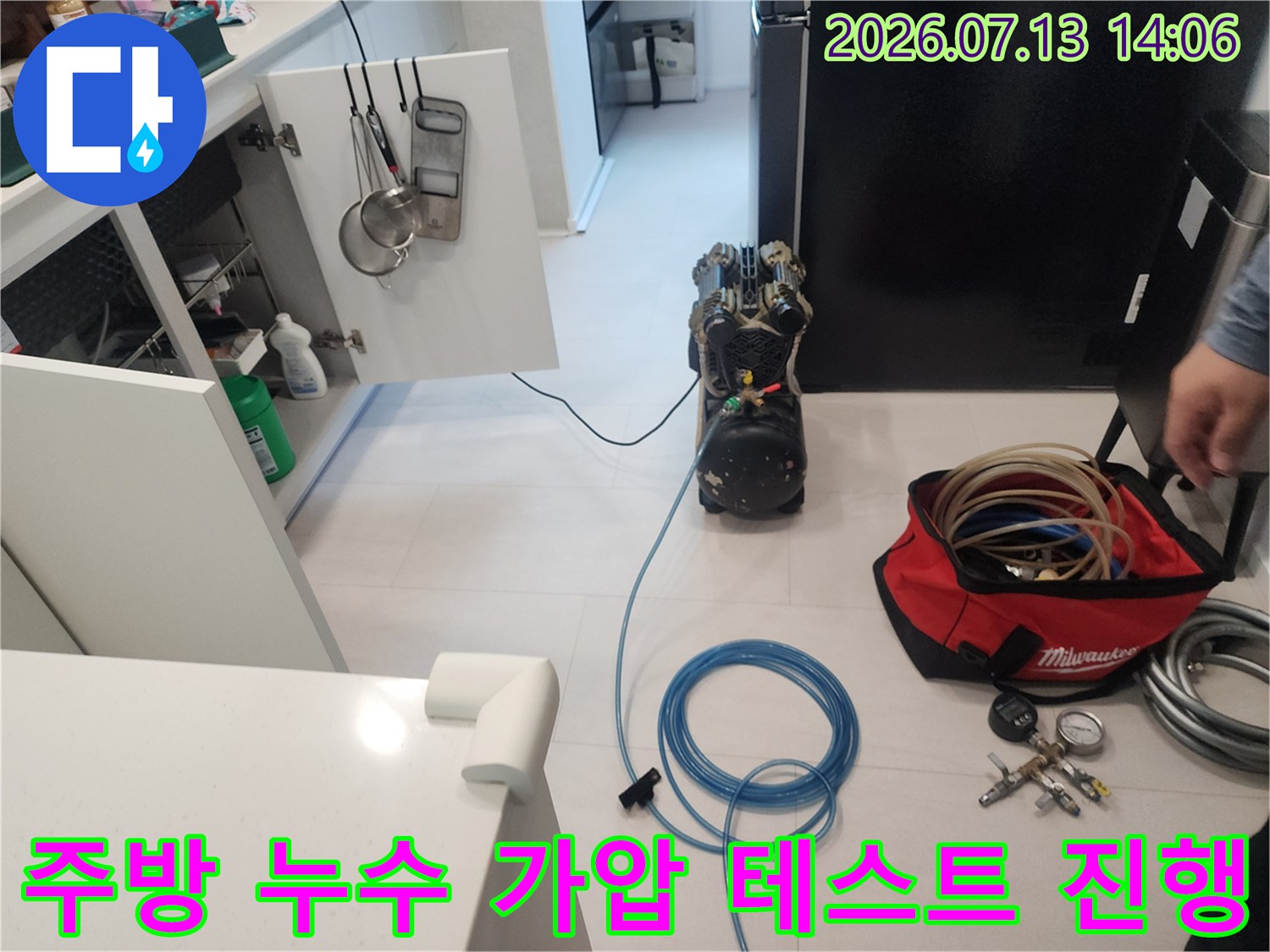 싱크대 하부장 앞에서 파란색 호스와 측정 장비를 사용하여 배관을 점검하는 장면