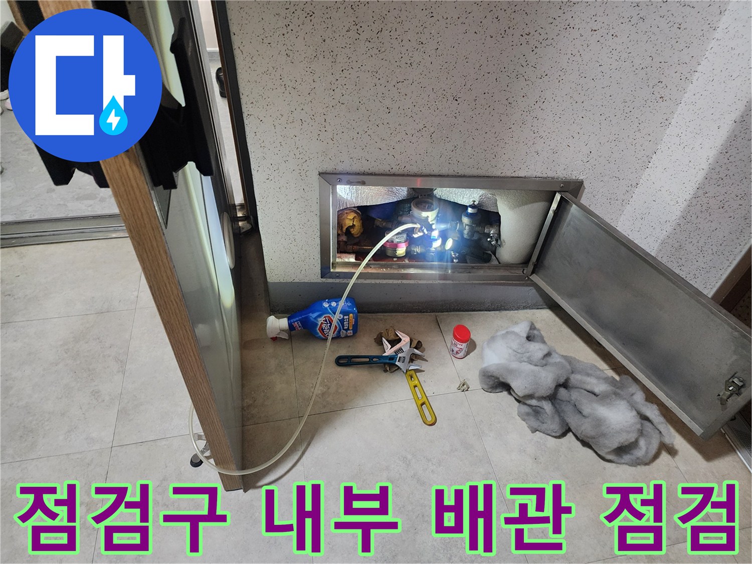 열려있는 점검구 안쪽의 배관 연결 상태와 측정 장비를 보여주는 사진입니다.