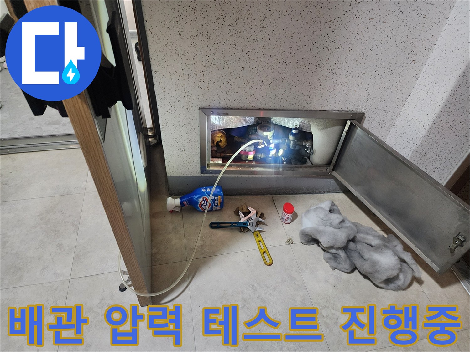 점검구 내부 배관에 연결된 파란색 호스와 측정 장비를 보여주는 사진입니다.