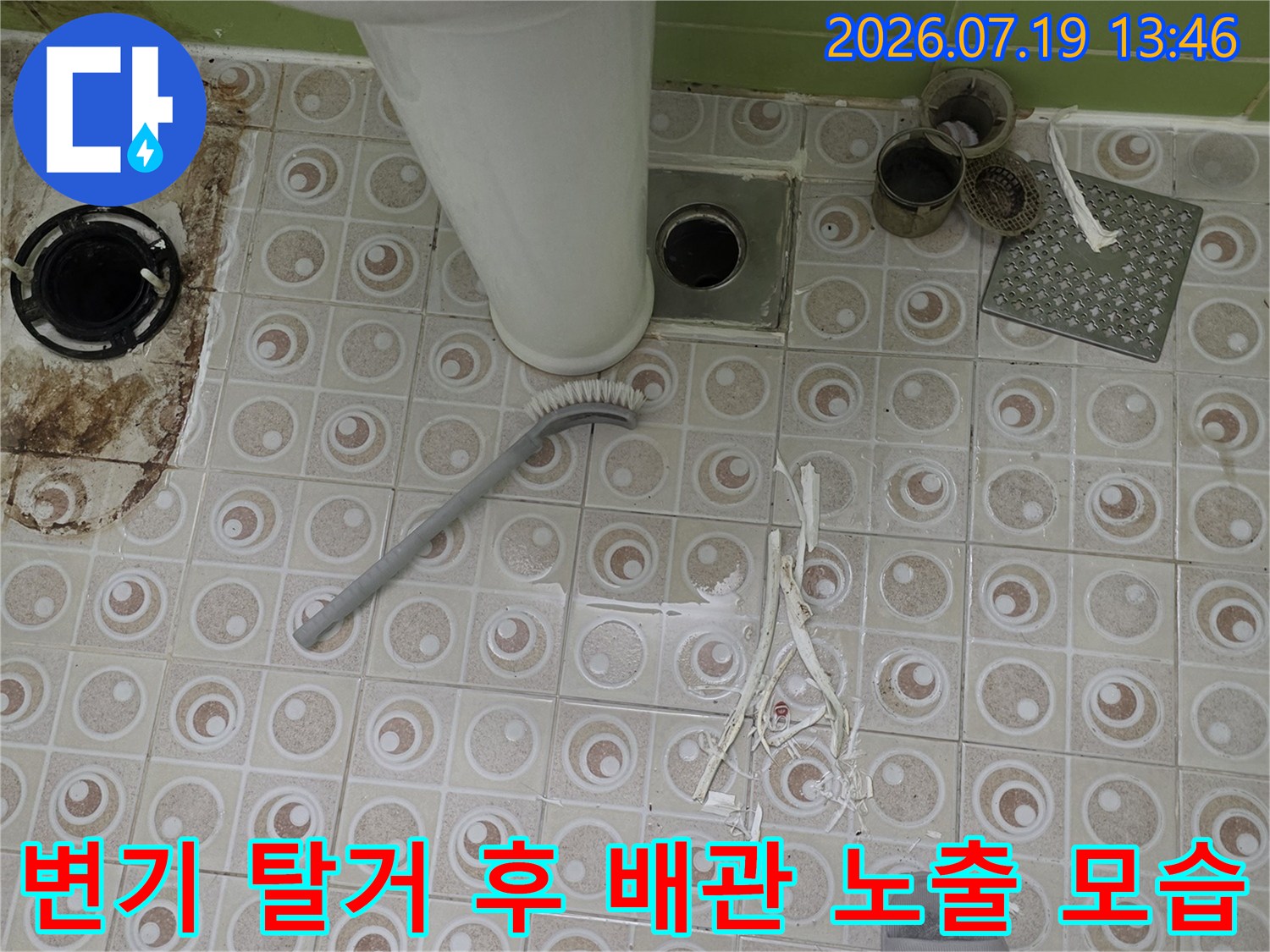 흰색 플라스틱 오수 배관이 바닥 타일 중앙에 위치하고 주변에 공구와 자재가 놓인 모습