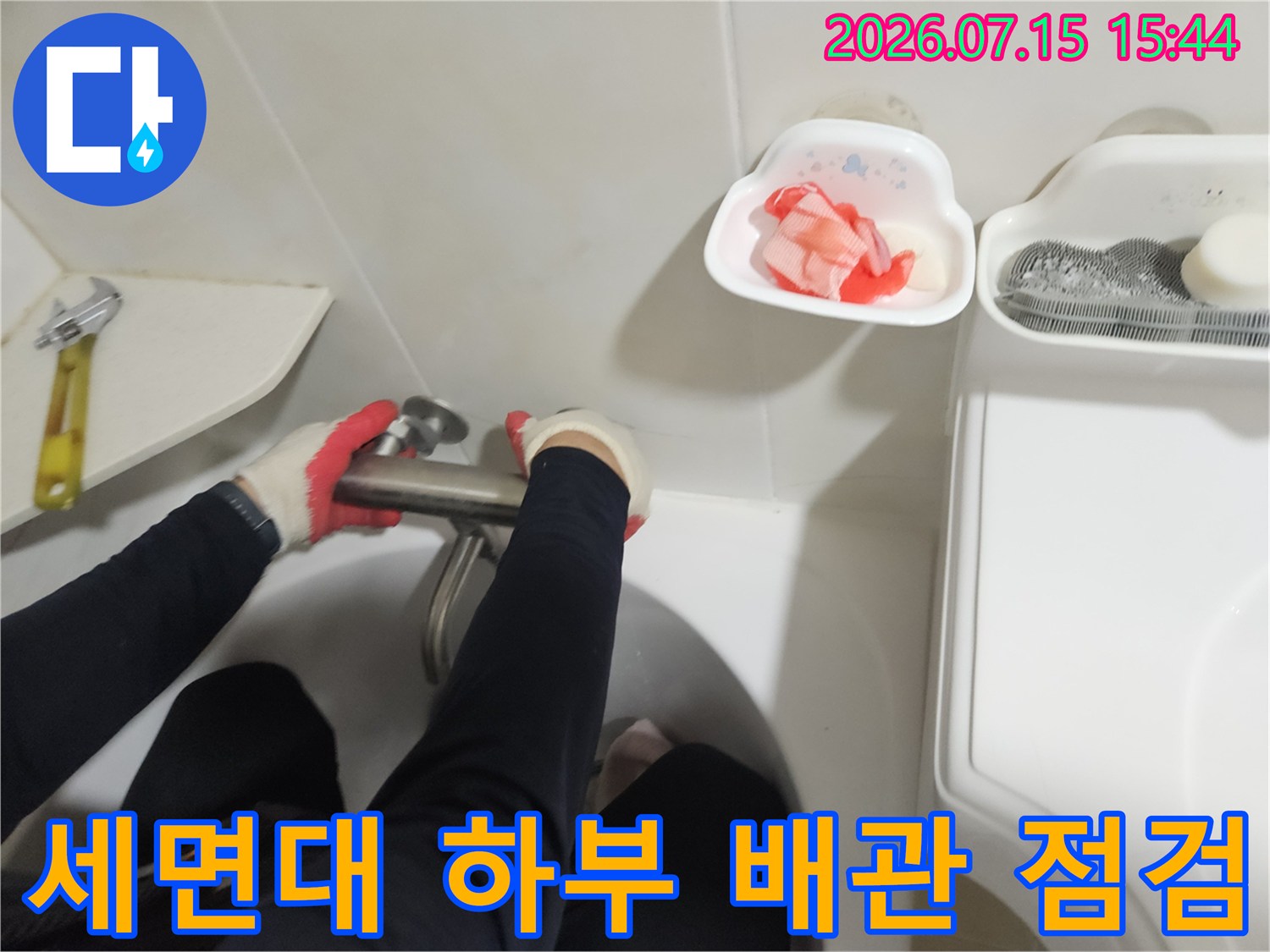 장갑을 착용한 작업자가 세면대 아래쪽 노출된 배관 부위를 점검하는 모습