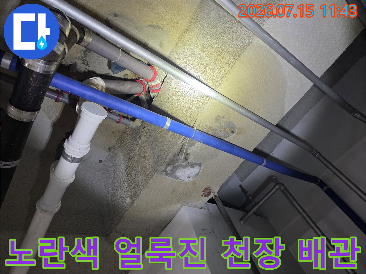 천장에 매달린 여러 가닥의 배관과 그 주변으로 넓게 퍼진 노란색 습기 자국