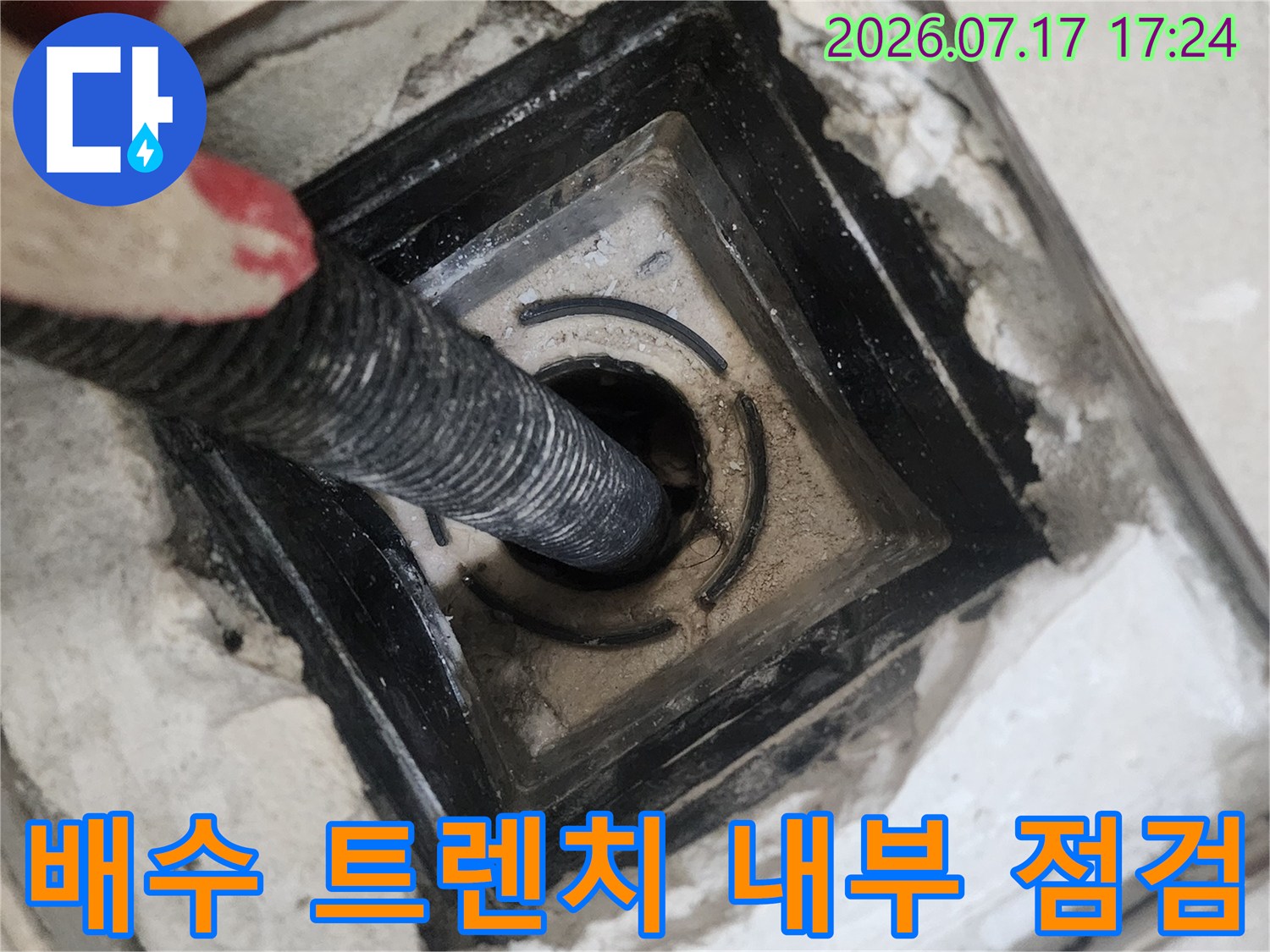 어두운 색상의 배수구 내부로 연결된 공압 테스트용 호스가 삽입된 모습