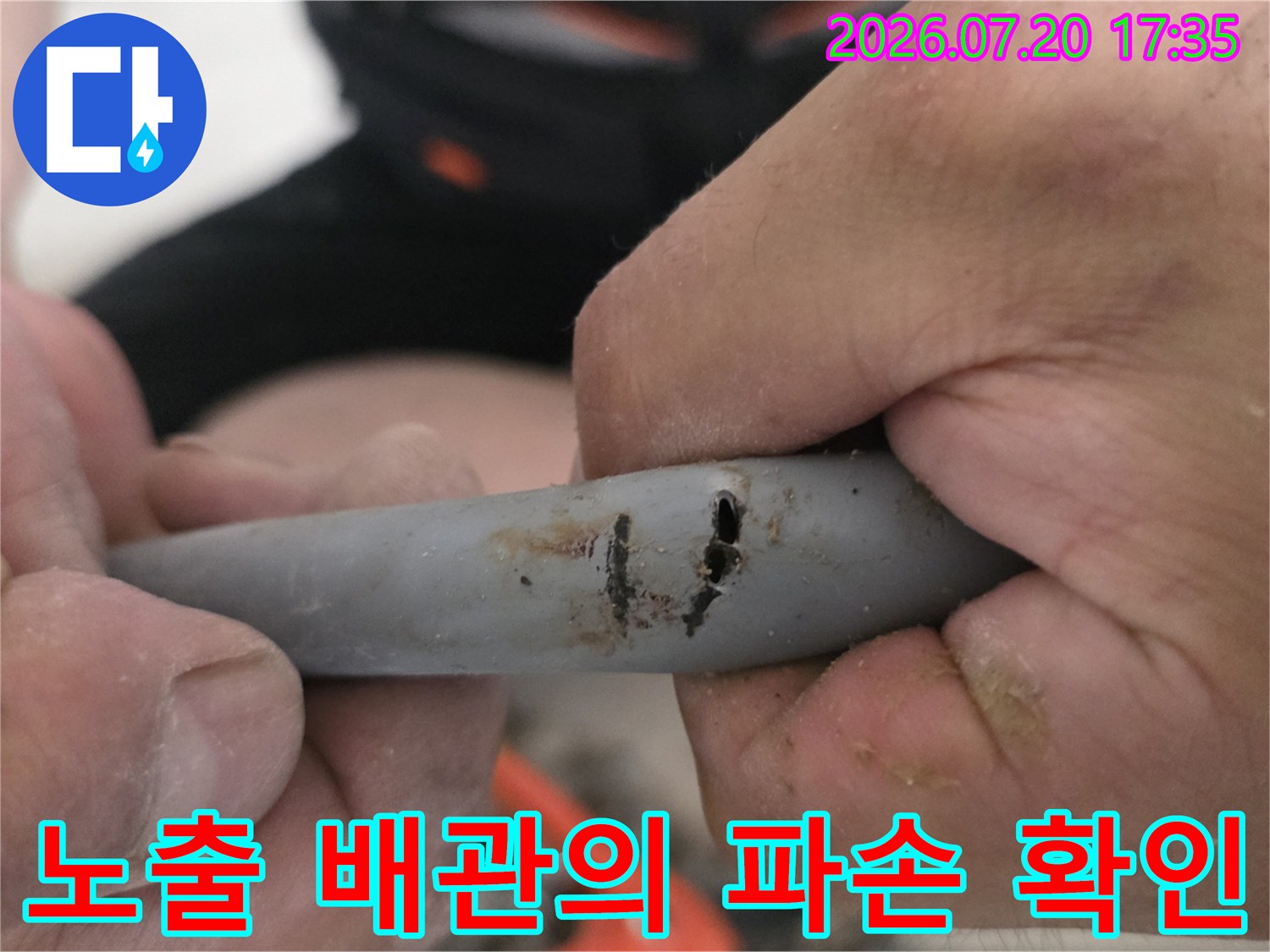 파손된 회색 배관 구간을 손으로 들어 올리며 점검하는 장면