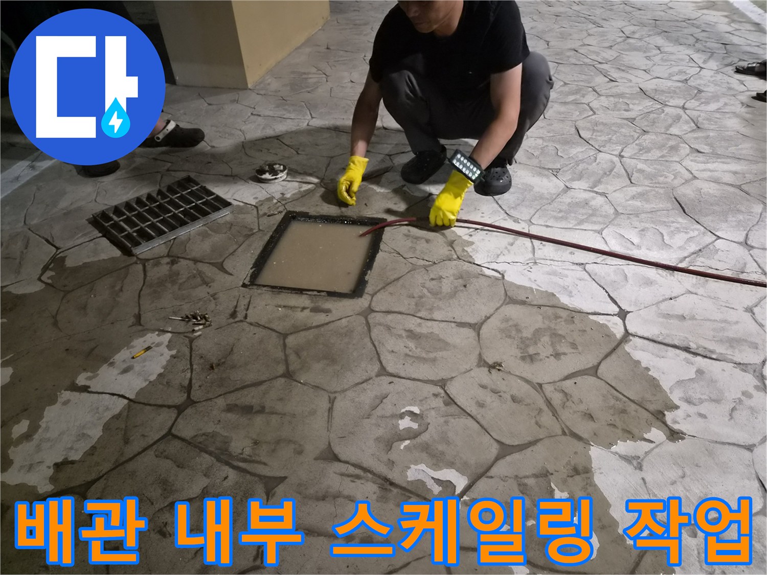 맨홀 덮개 옆으로 붉은색 배관 청소용 케이블을 넣고 있는 현장 사진