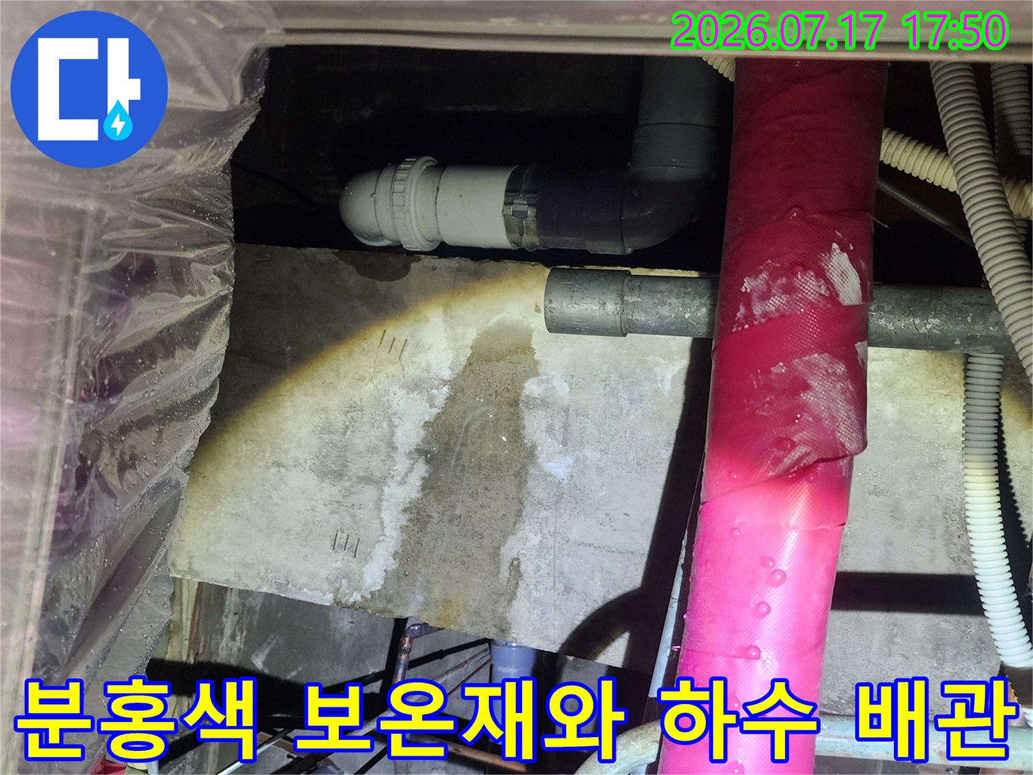천장 속에 설치된 분홍색 보온재 배관과 회색의-배수 연결관 모습