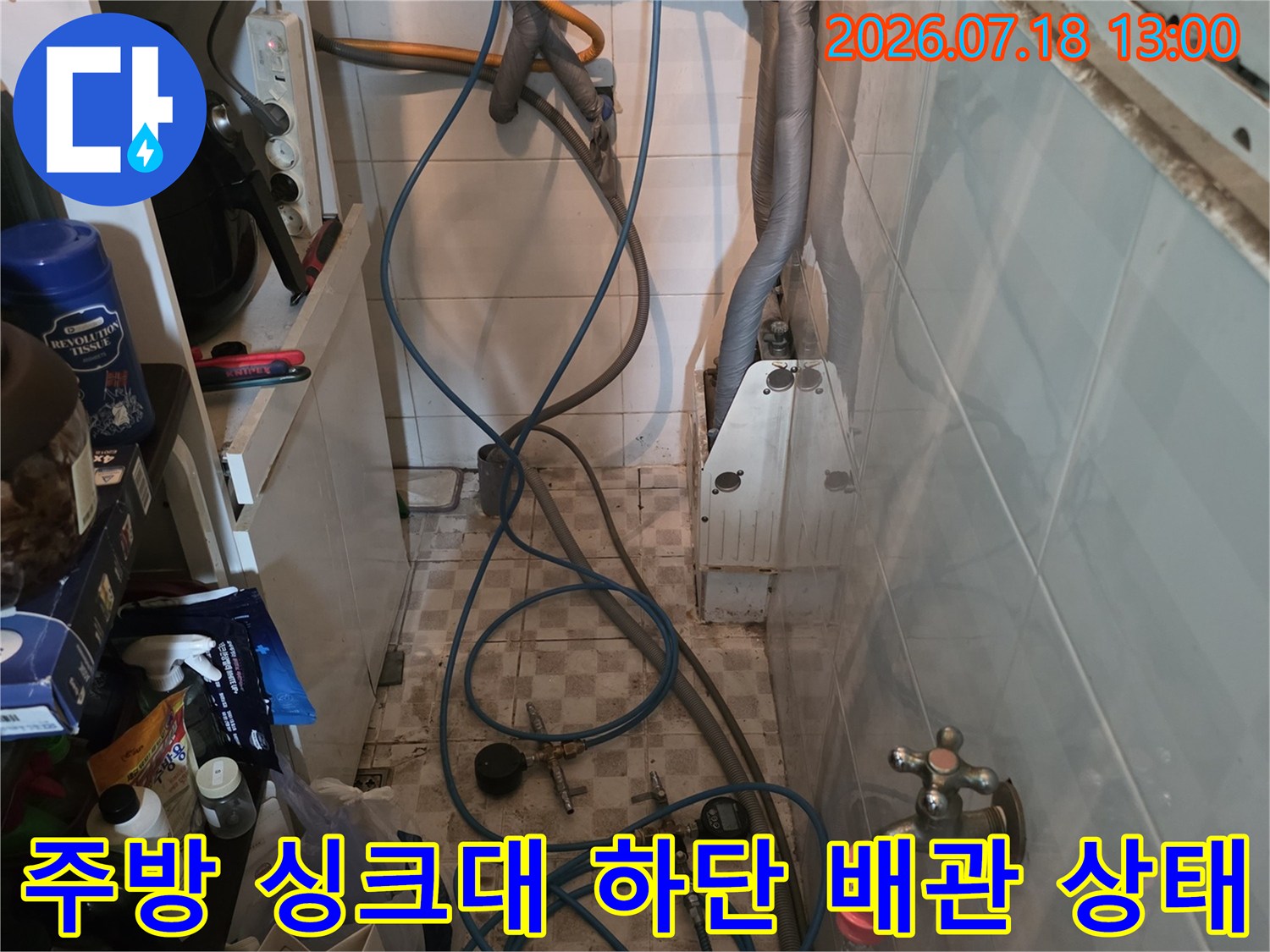싱크대 아래쪽-다양한 색상의 호스와 수도 밸브가 복잡하게 연결된 주방 하부 모습