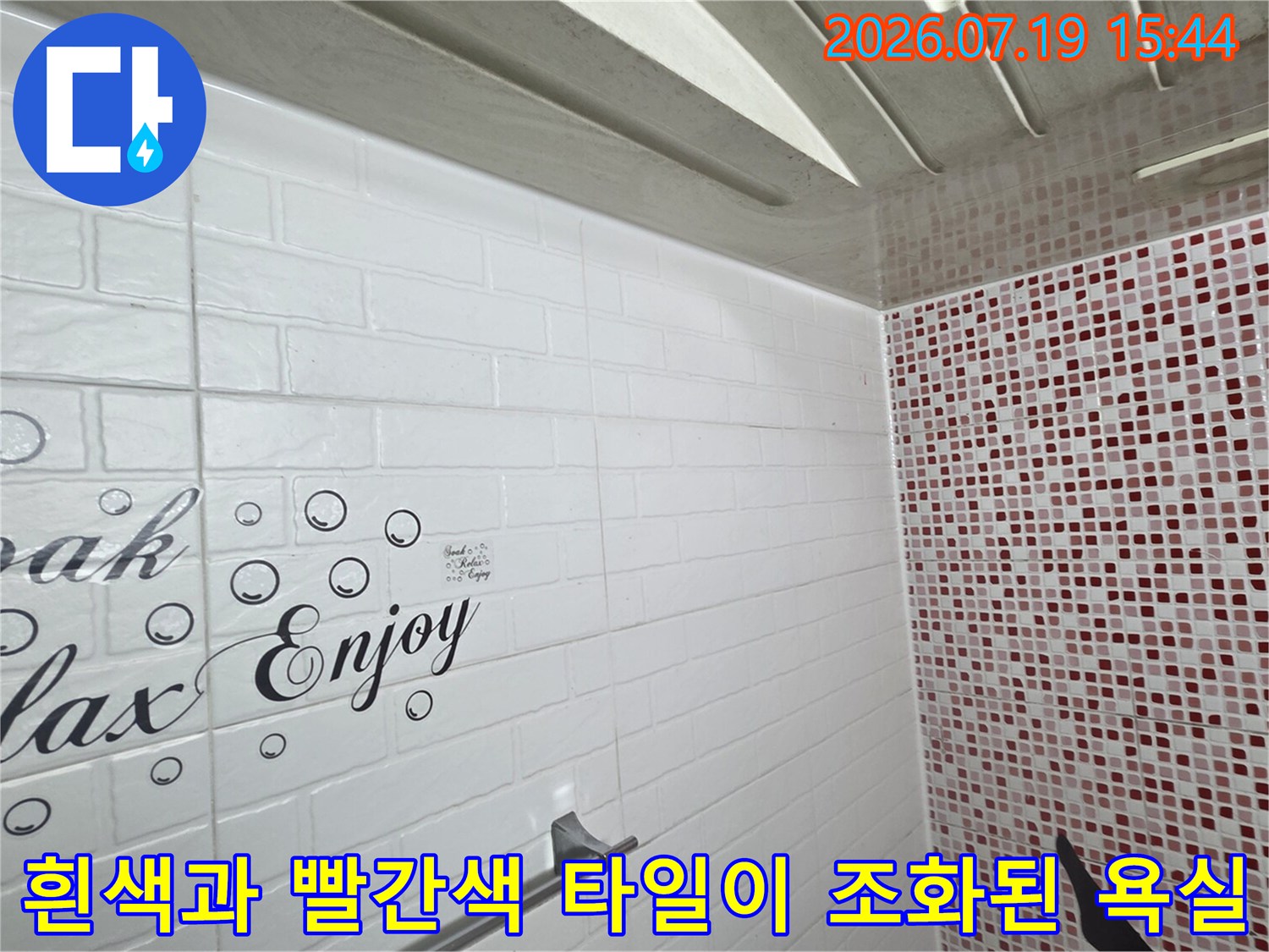 가로형 흰색 타일에 장식 문구가 있고 우측에는 붉은색 모자이크 타일이 시공된 화장실 벽면 사진