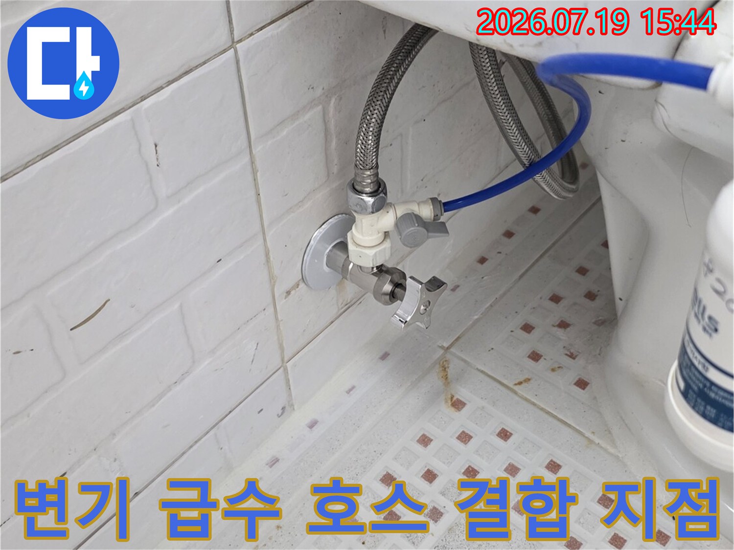 격자 패턴 타일 벽면의 변기 밸브와 파란색 플라스틱 호스-연결 부위