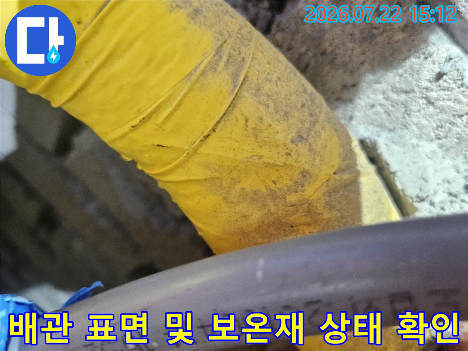 회색의 매끄러운 수도 배관과 노란색 비닐 소재의 보온재가 설치된 천장 내부 모습