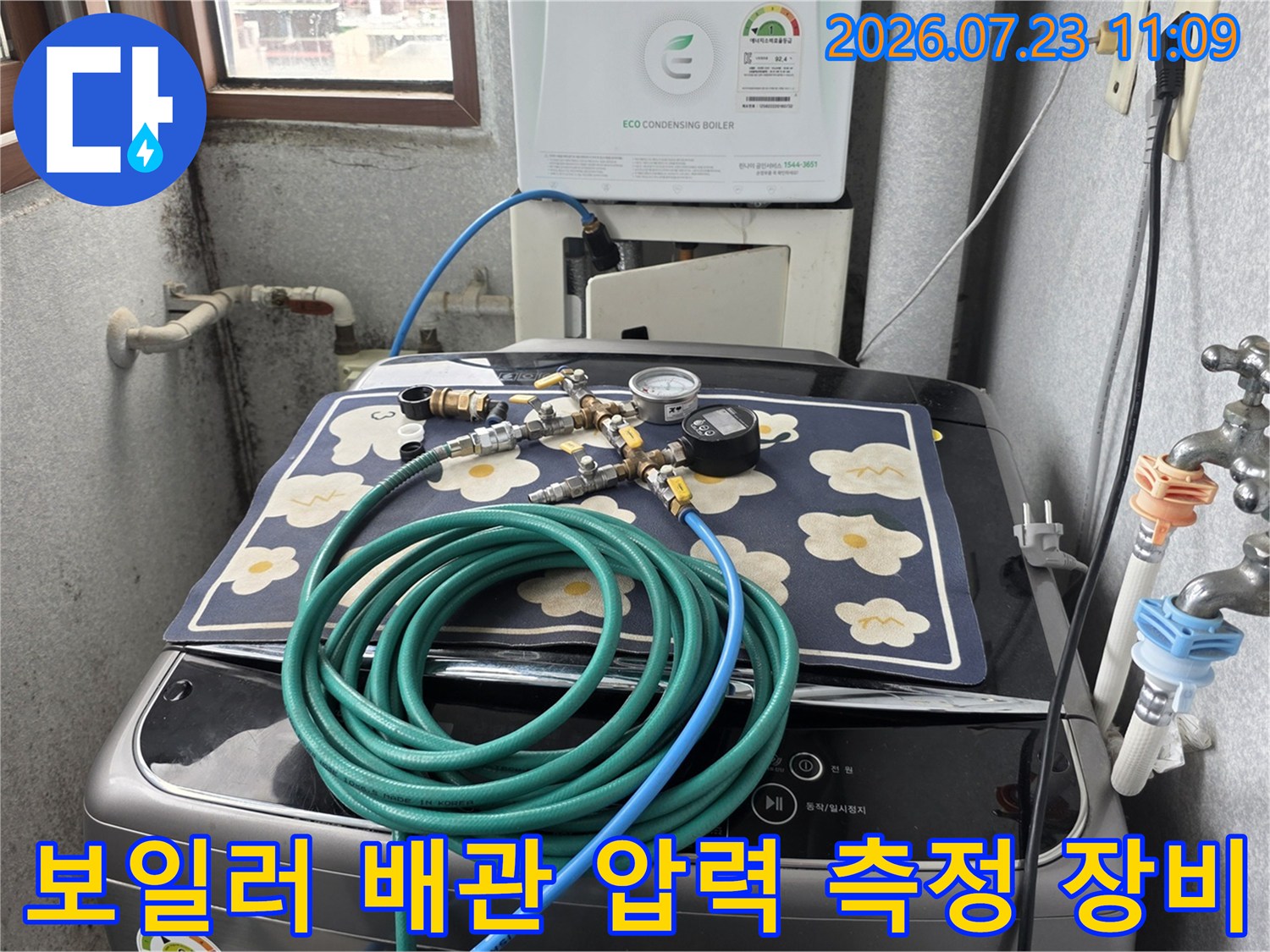 세탁기 위에 놓인 꽃무늬 매트와 누수 점검용 압력 게이지-호스 연결 상태