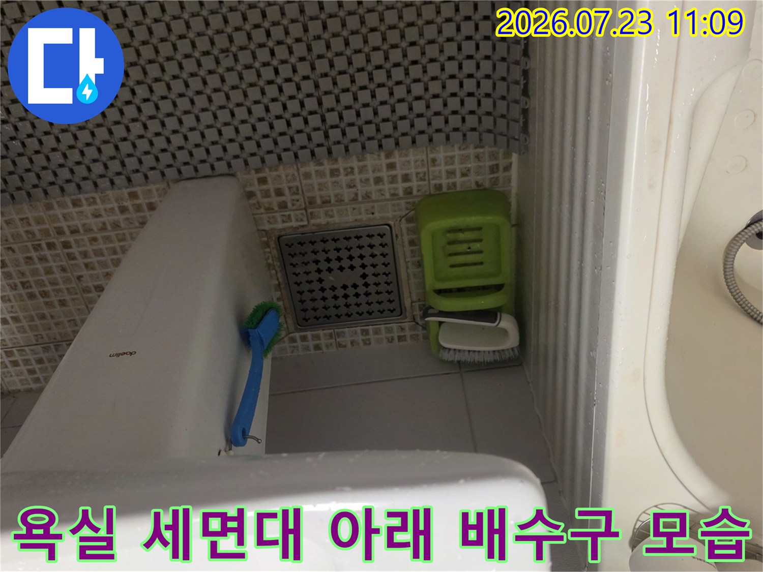 흰색 도기 세면대 하단의 타일 바닥과 사각형 모양의 배수구가 찍힌 사진
