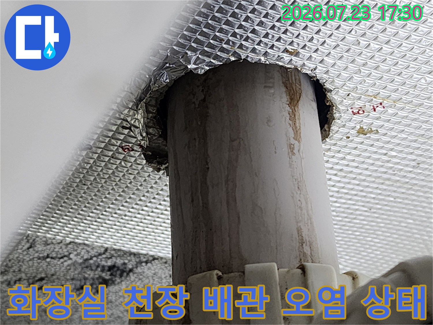 은색 단열재가 설치된 화장실 천장에서 회색 배관을 통해 누수가 발생하여 얼룩이 진 모습