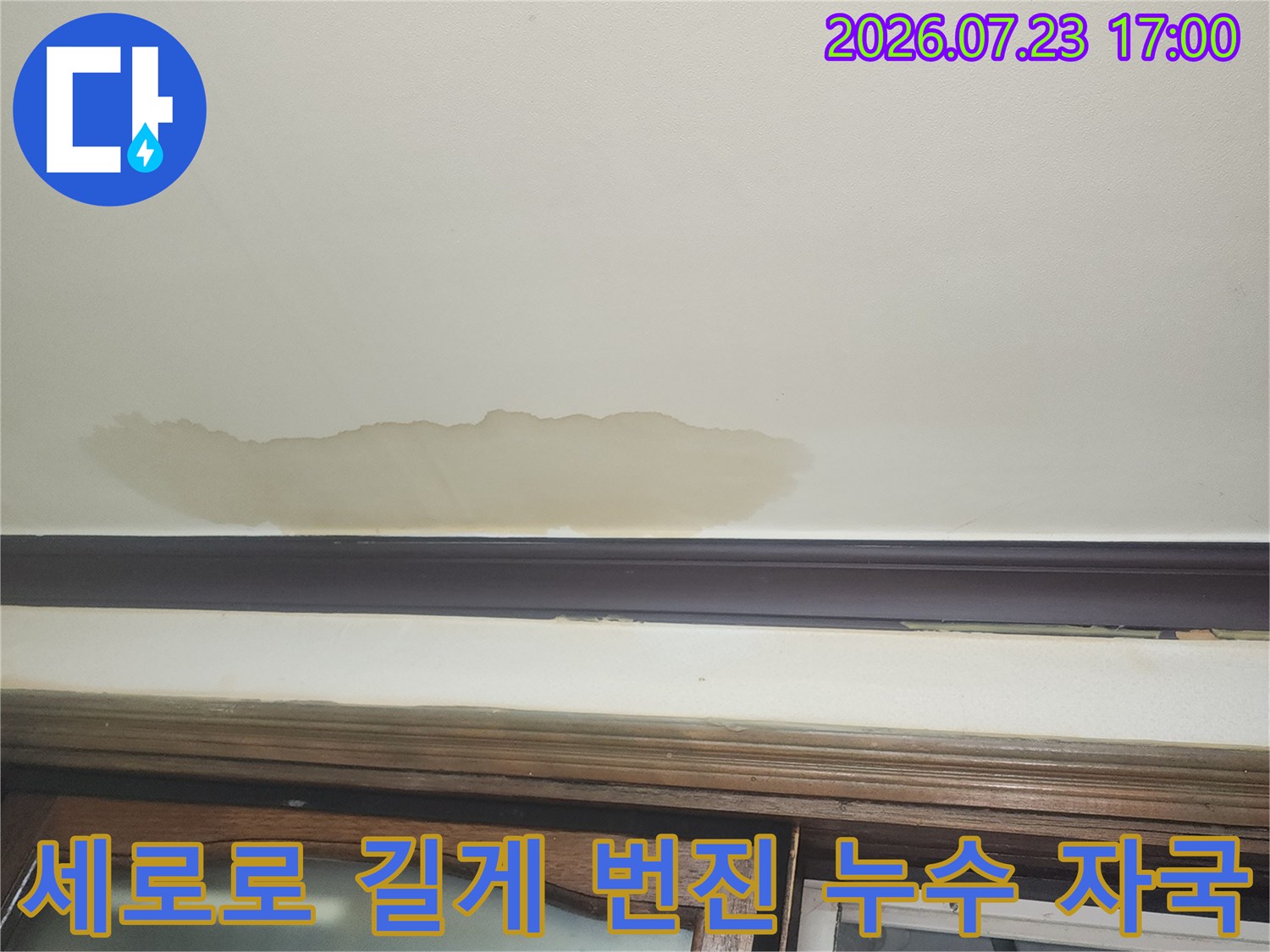 창틀 옆 벽지에 발생한 세로 형태의 짙은 갈색 누수 오염 부위