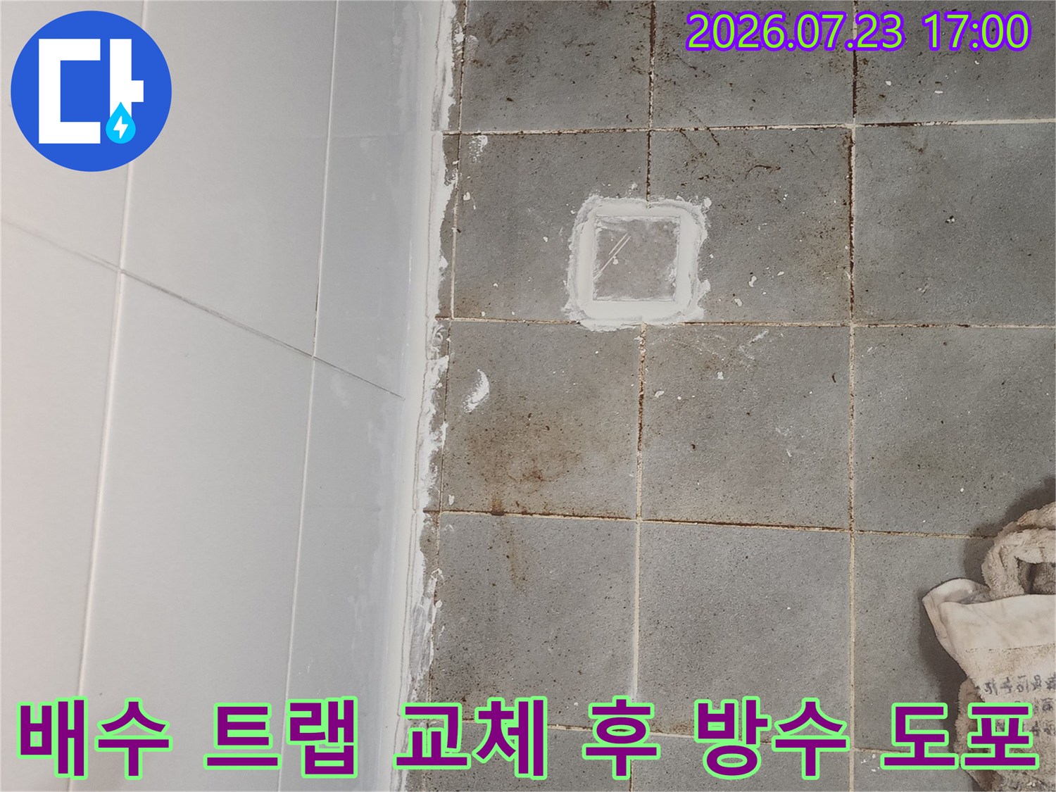 회색 타일 바닥의 배수구 구멍 주변에 하얀색 보수재가 발라져 있는 사진