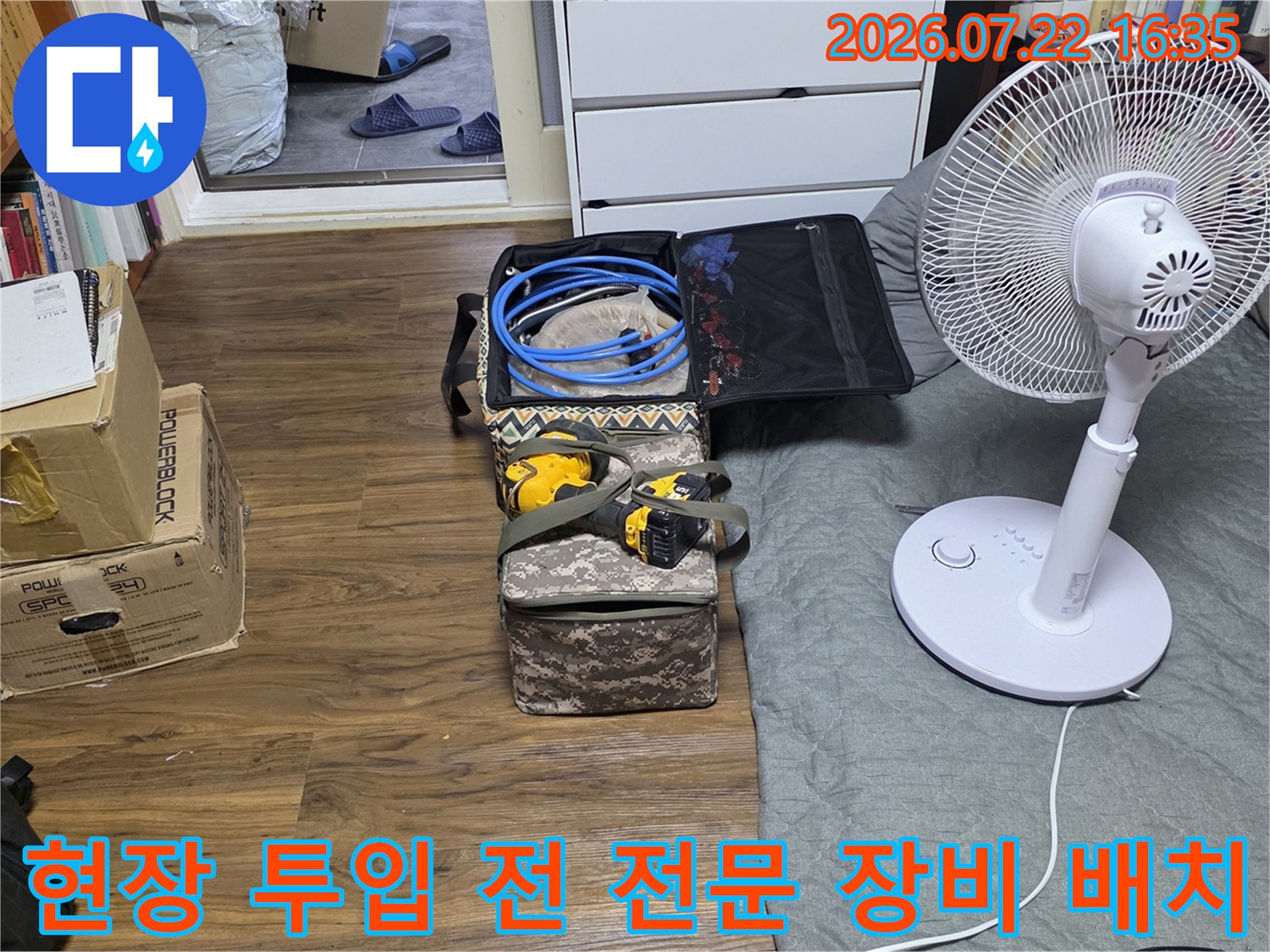 바닥에 놓인 누수 탐지용 파란 호스와 드릴-옆에는 흰색 선풍기가 세워져 있음