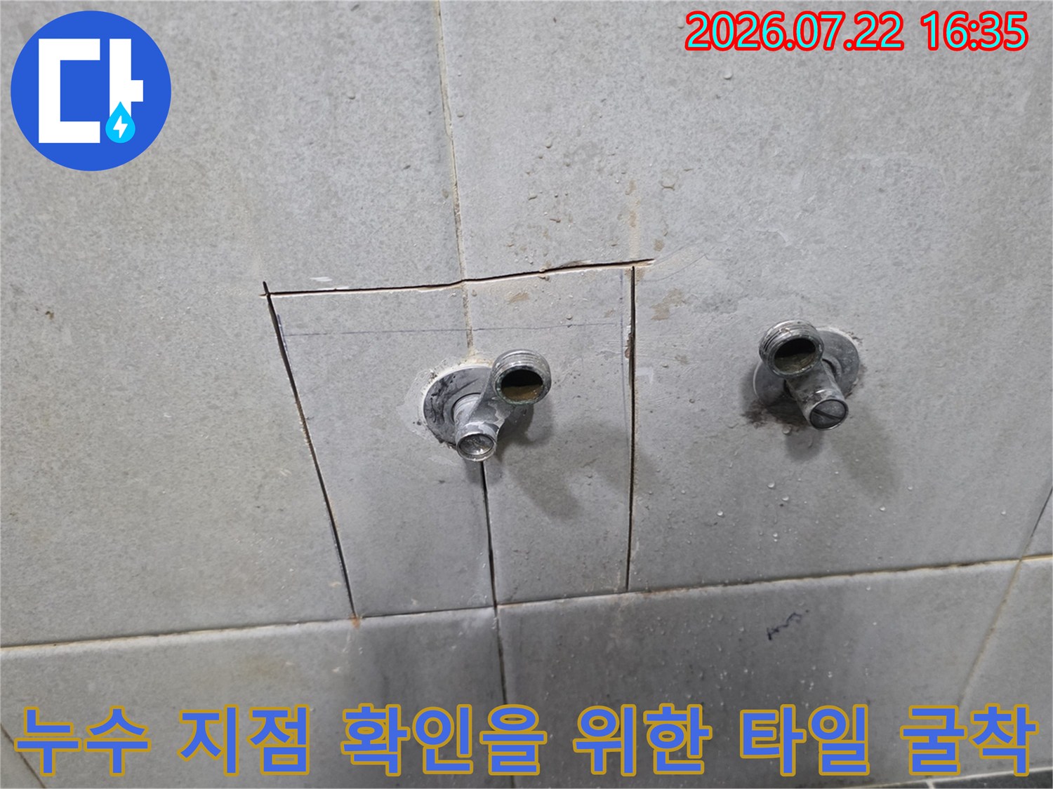 타일 벽면에 직사각형 형태로 구멍이 뚫려 있고 내부 수도 배관 두 개가 돌출된 모습