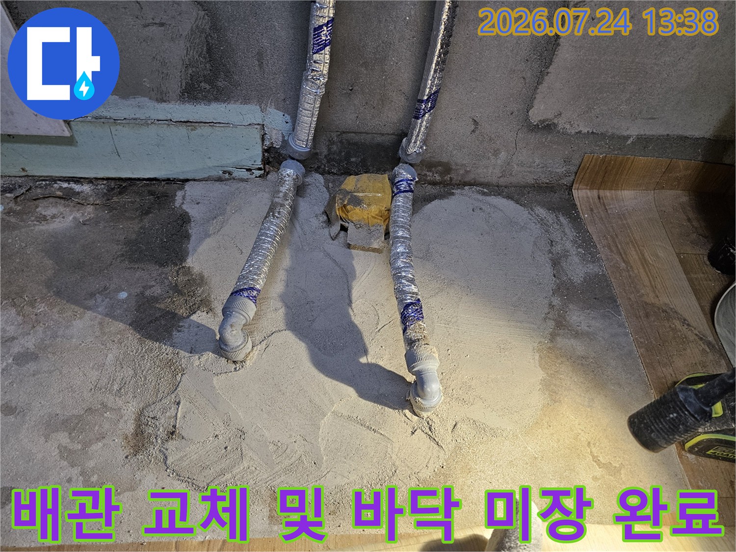새로운 배관 두 개가 나란히 배치되어 있고 하단이 시멘트로 마감된 현장 사진