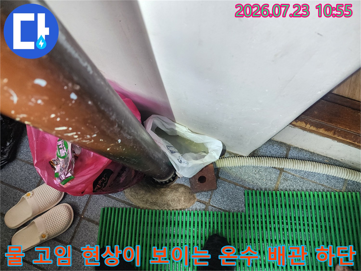 바닥 타일 위로 누수된 물이 고여 있고 배관 주변에 임시 조치 흔적이 보이는 사진