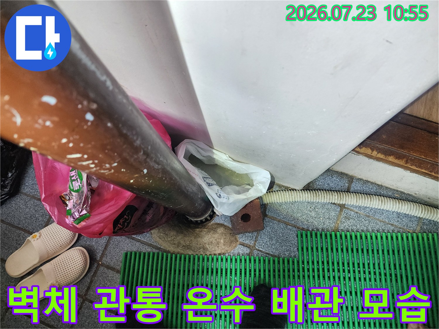 흰색 벽체를 통과하여 바닥으로 연결된 금속 재질의 온수 배관-누수 점검 부위