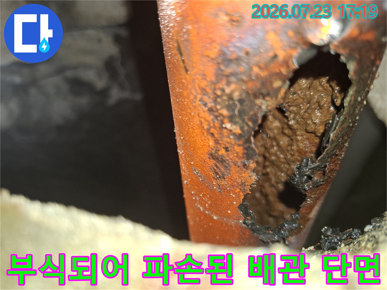 오렌지색 배관의 측면이 부식으로 인해 뚫려 있는 누수 지점 근접 사진