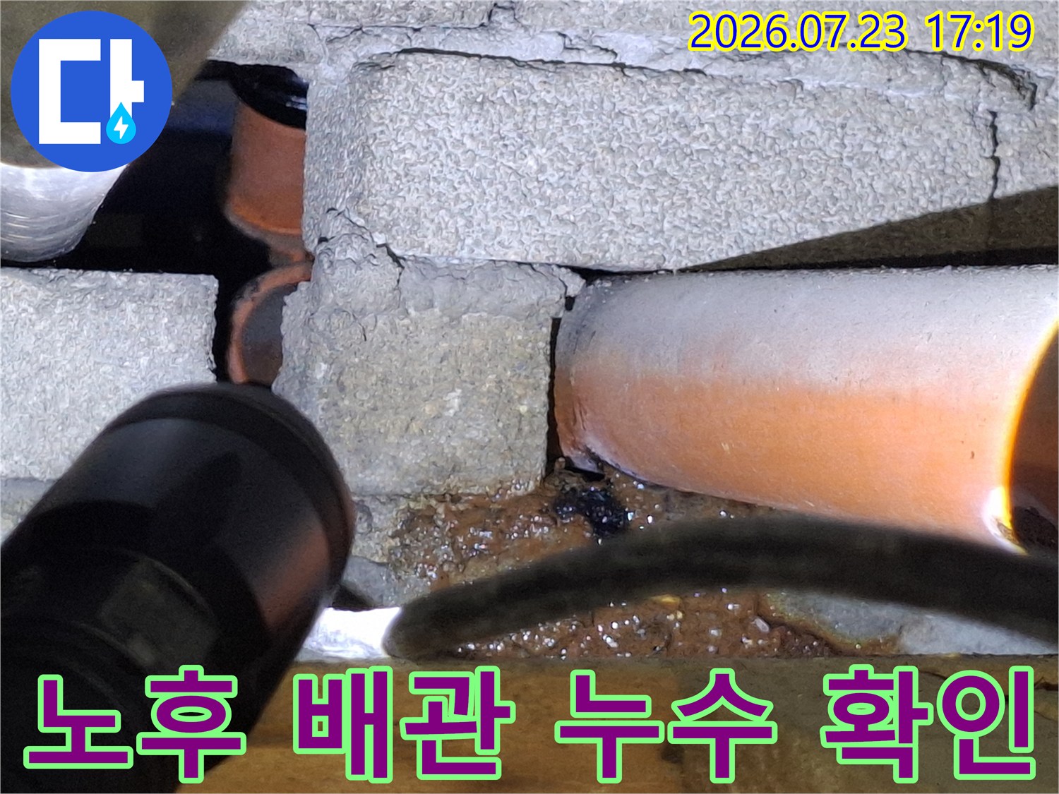 회색 콘크리트 구조물 사이에 설치되어 부식이 진행된 오렌지색 배관의 모습