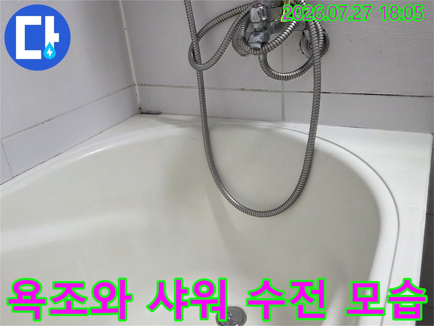흰색 타일 벽면에 설치된 은색 샤워기 호스가 욕조 위로 내려온 장면