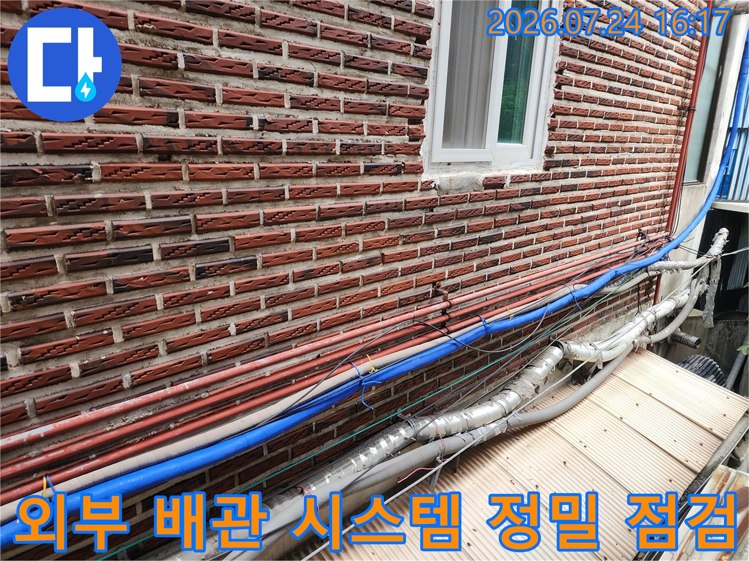 벽돌 벽면과 수평으로 이어진 파란색 및 은색 마감의 수도 노출 배관
